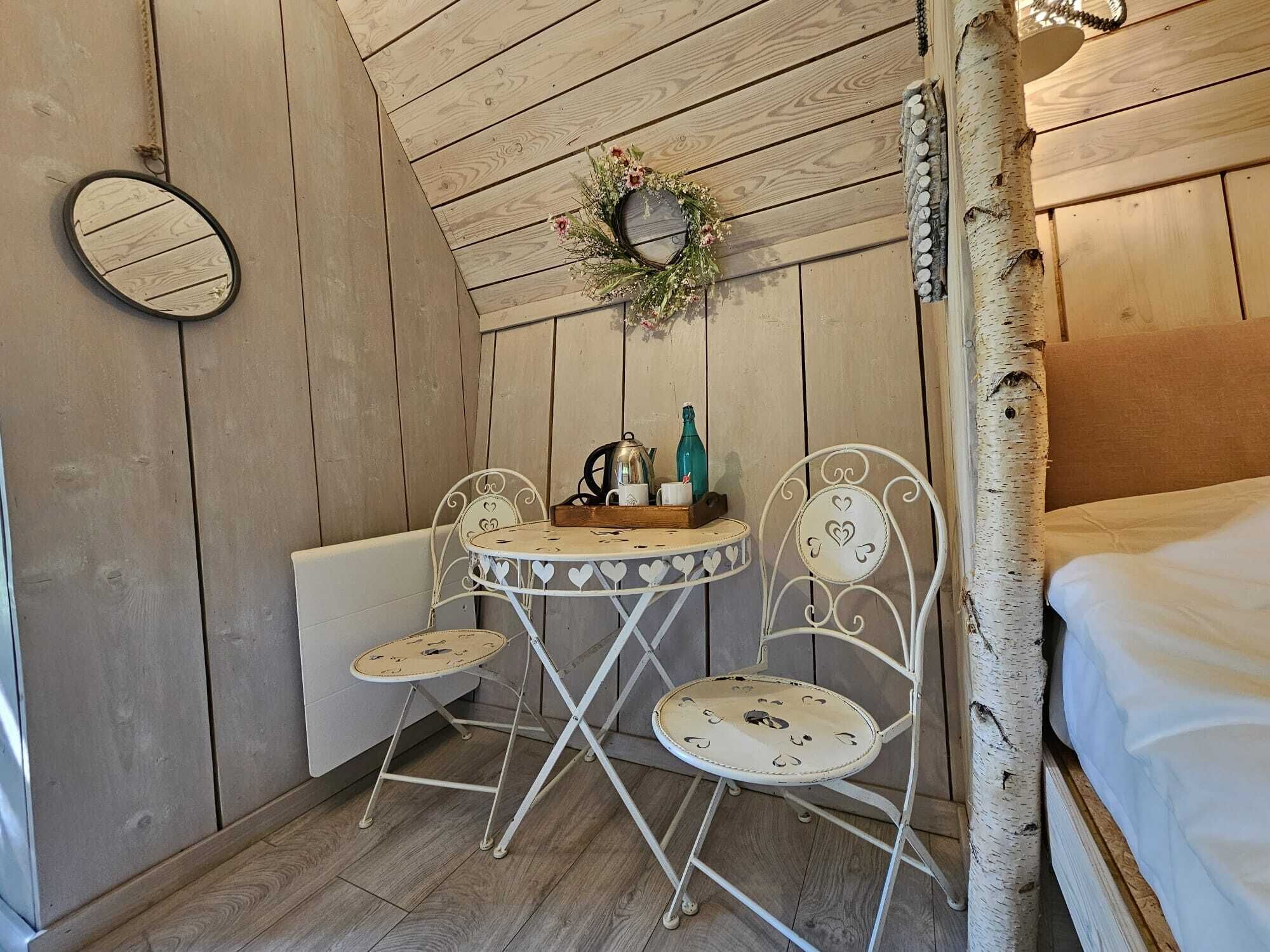 A cozy room with a wooden ceiling, a round table with chairs, a bed, and a mirror on the wall.