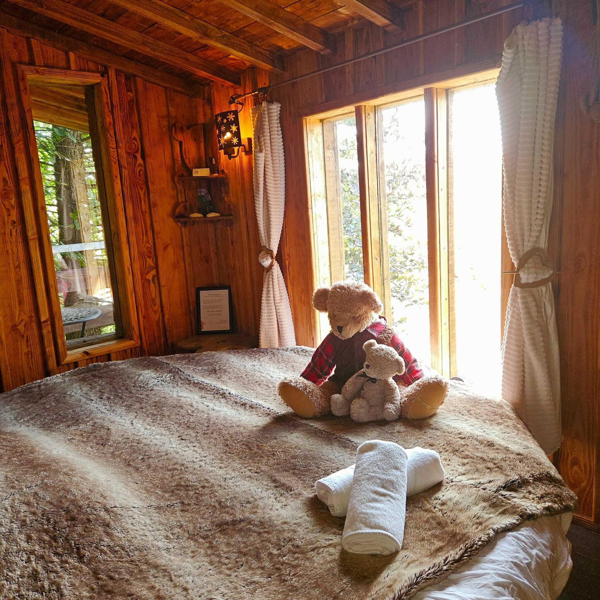 A cozy room with a large bed, a teddy bear, and a window with curtains.
