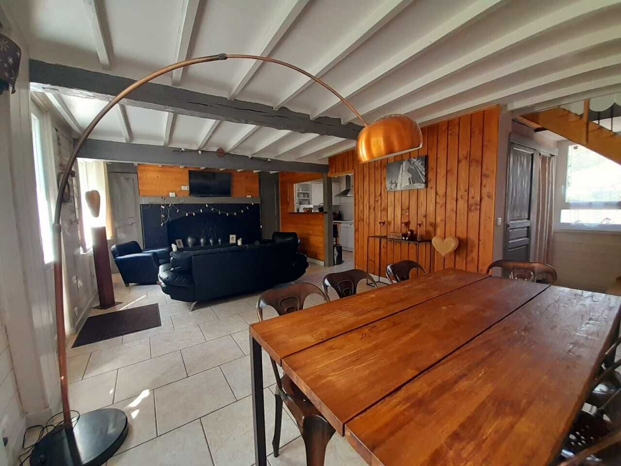 Amplia sala de estar con una mesa de comedor de madera, un sofá y una cocina al fondo.