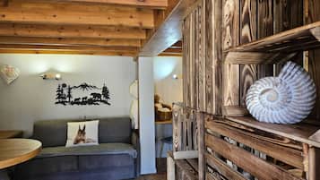 A cozy room with a wooden ceiling, a sofa with a pillow, a wall with a nature-themed decal, and a shelf with a seashell.