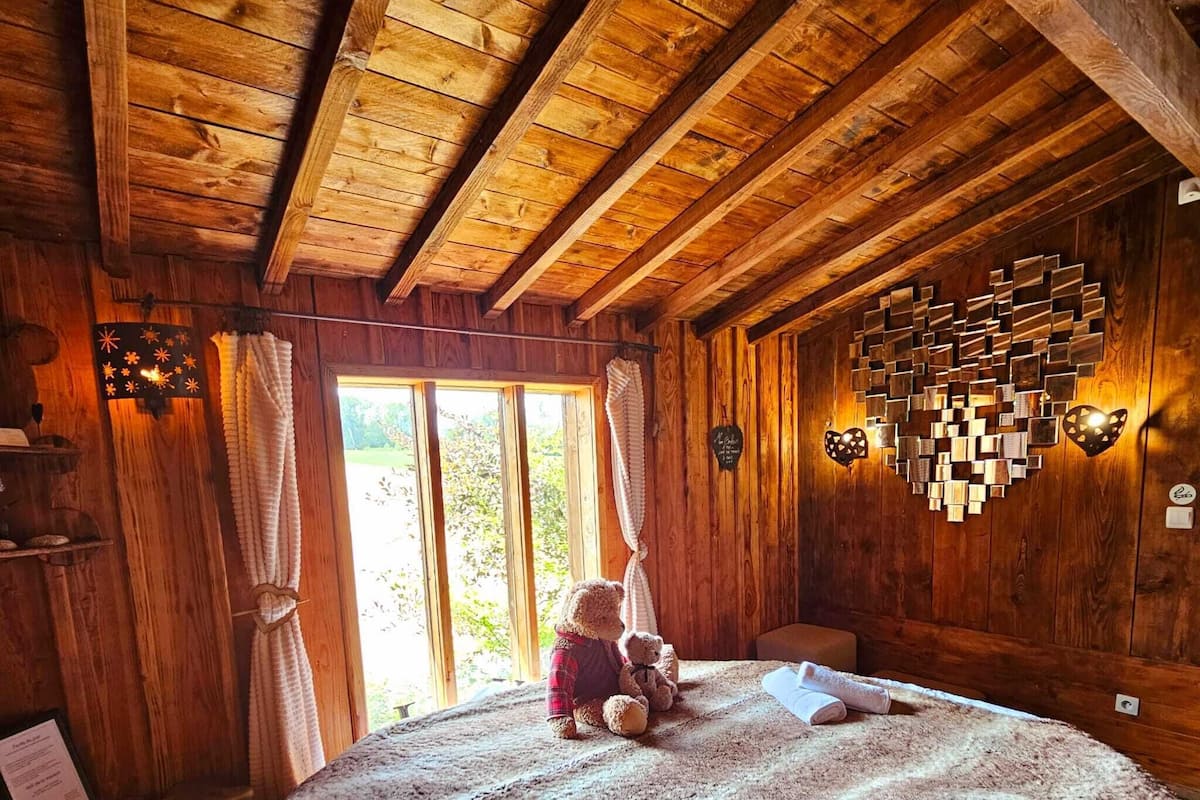 Een houten kamer met een bed, een teddybeer en een decoratieve hartvormige versiering aan de muur.