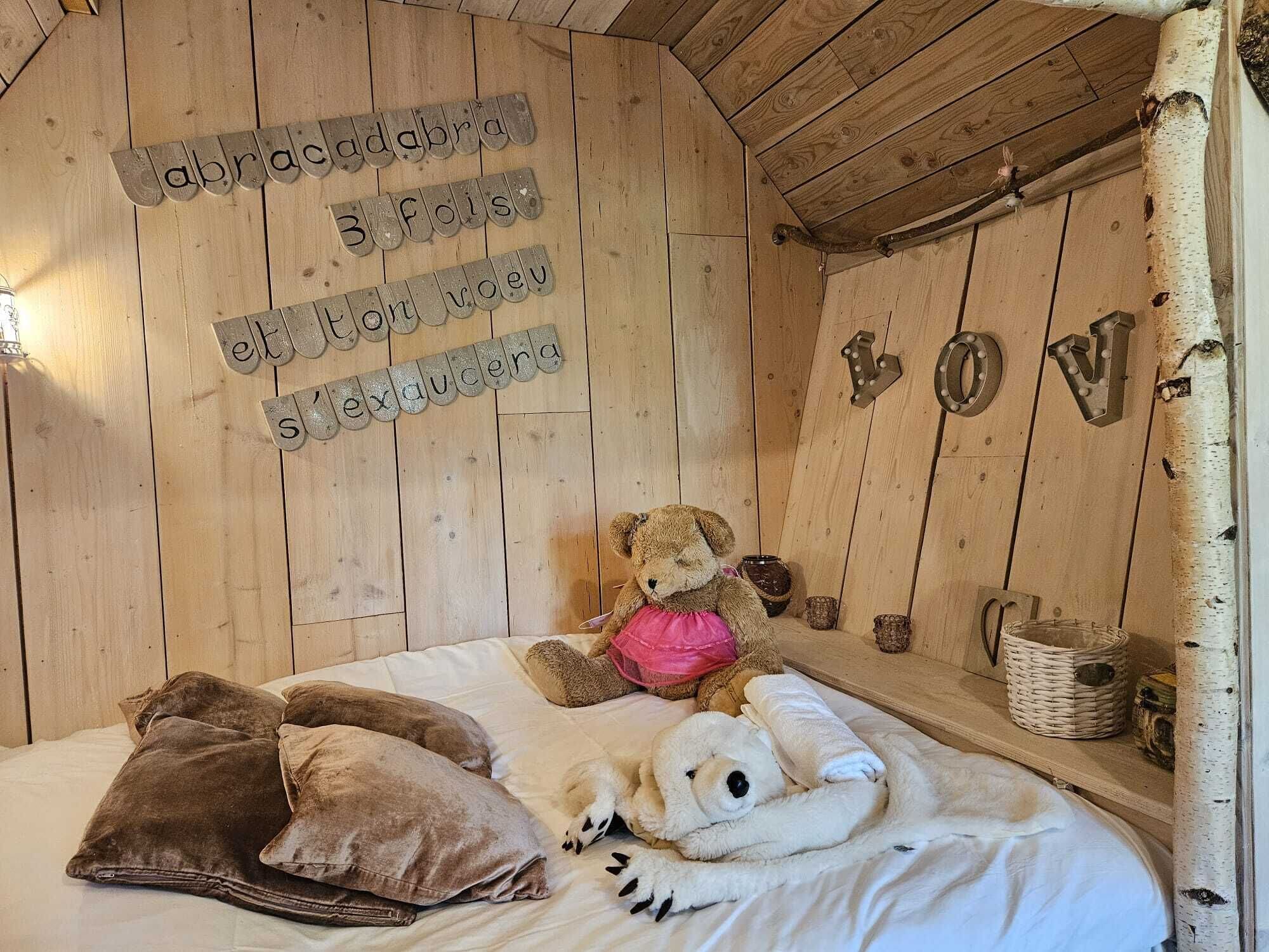 Una habitación acogedora de madera con una cama, dos ositos de peluche y una pared con letras de madera que deletrean una frase.