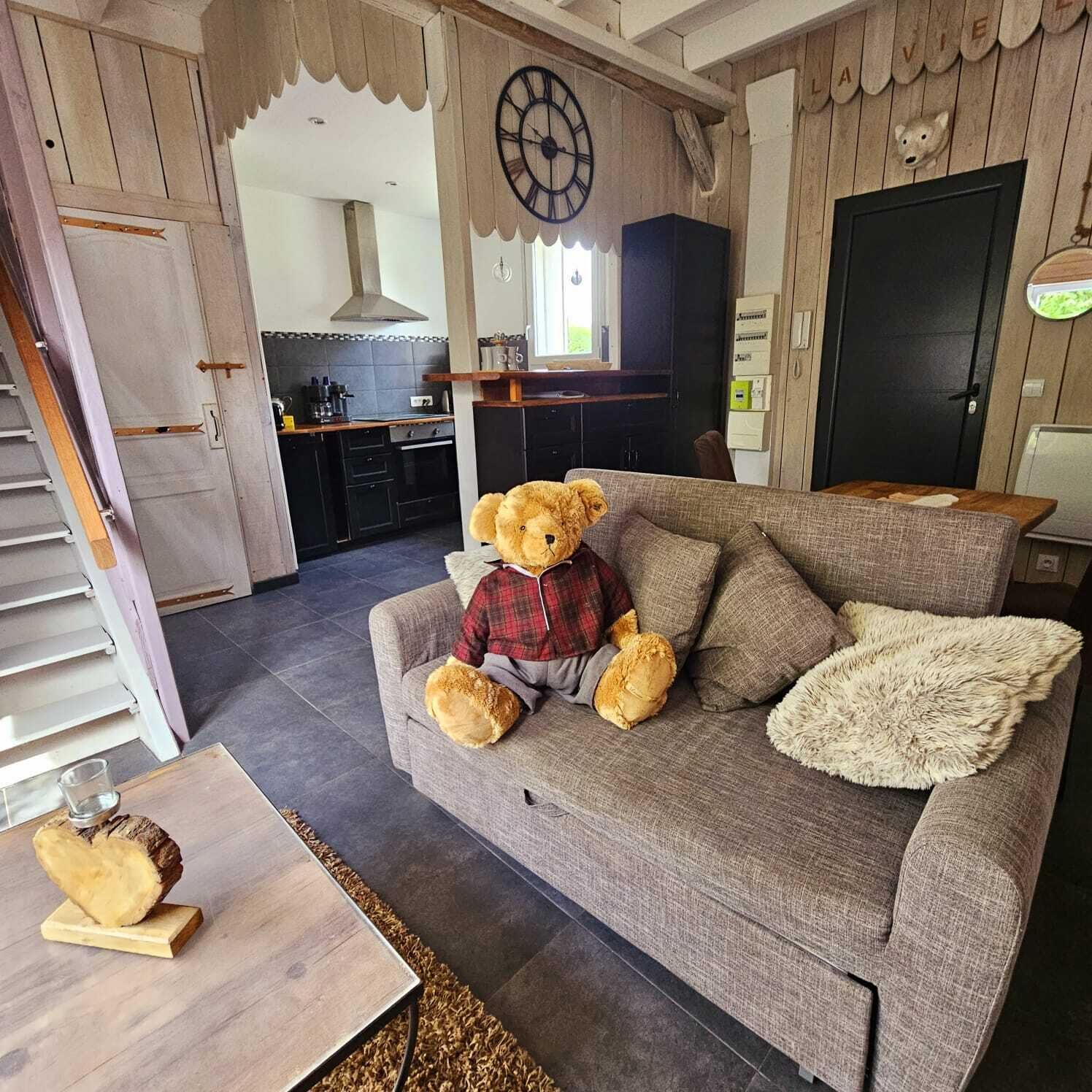 A cozy living room with a grey sofa, a teddy bear dressed in a plaid shirt, and a fluffy throw blanket.