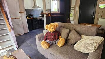 A cozy living room with a grey sofa, a teddy bear dressed in a plaid shirt, and a fluffy throw blanket.