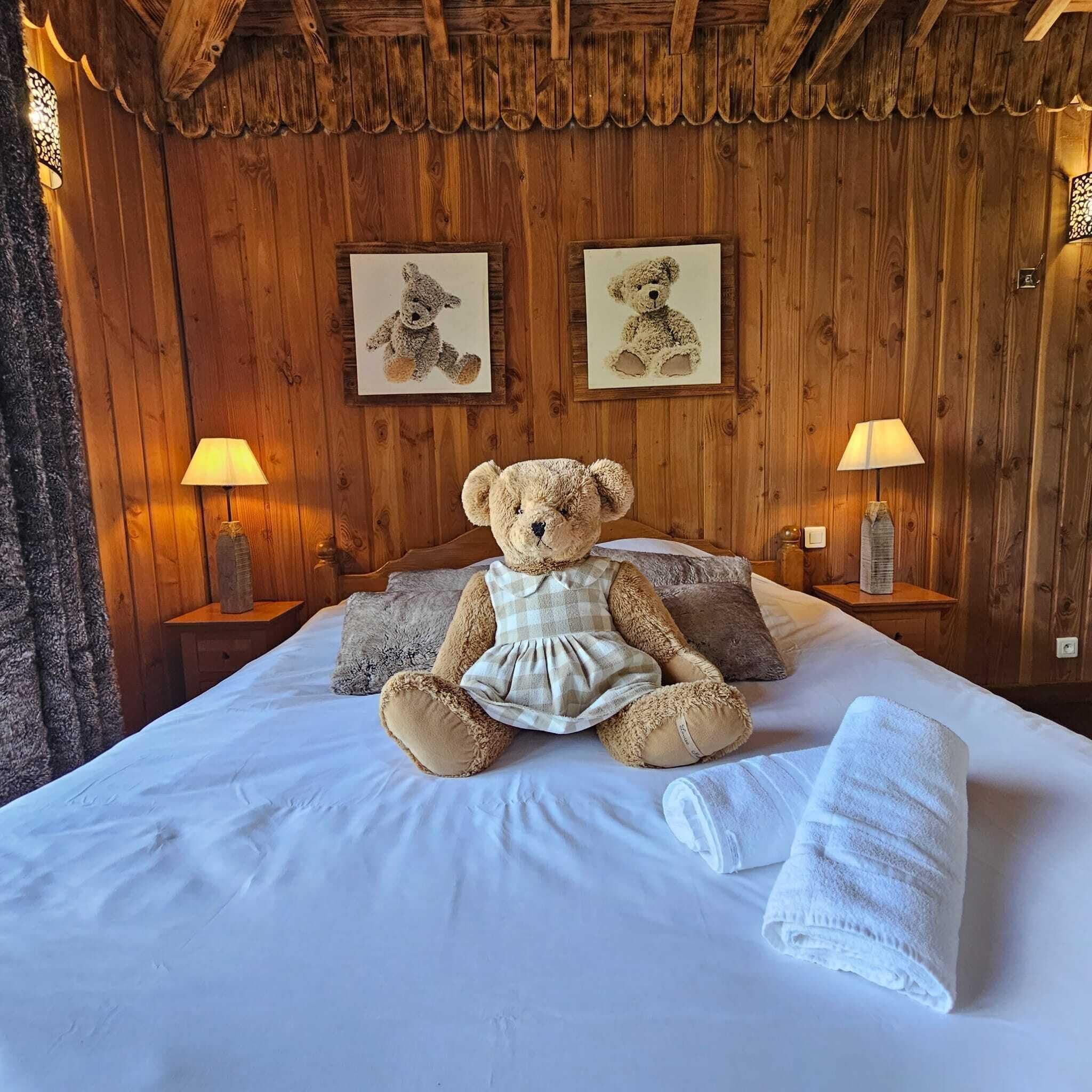 A cozy bedroom with a large bed, a teddy bear, two framed pictures, and two bedside lamps.