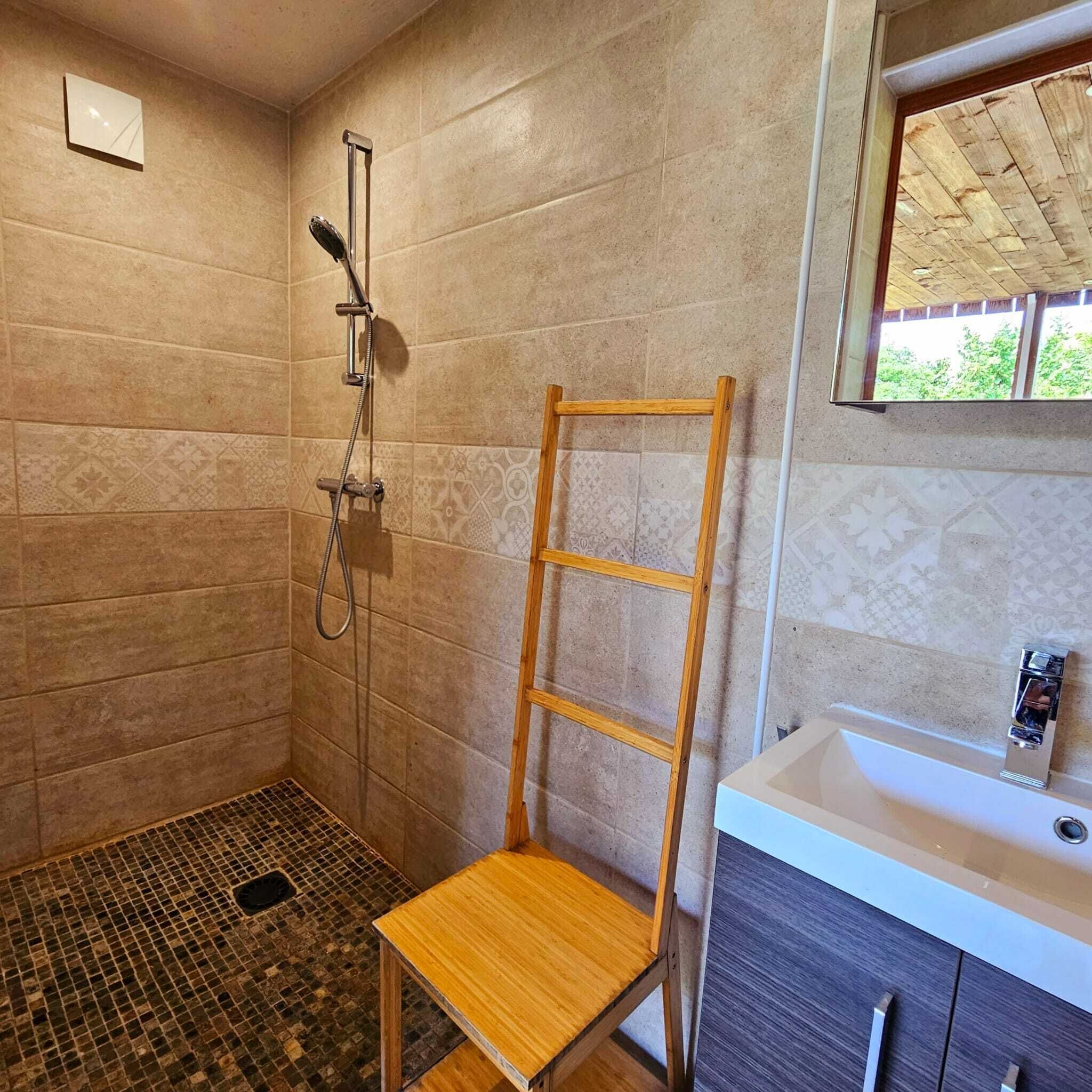 A bathroom with a shower, a wooden shelf, and a sink.