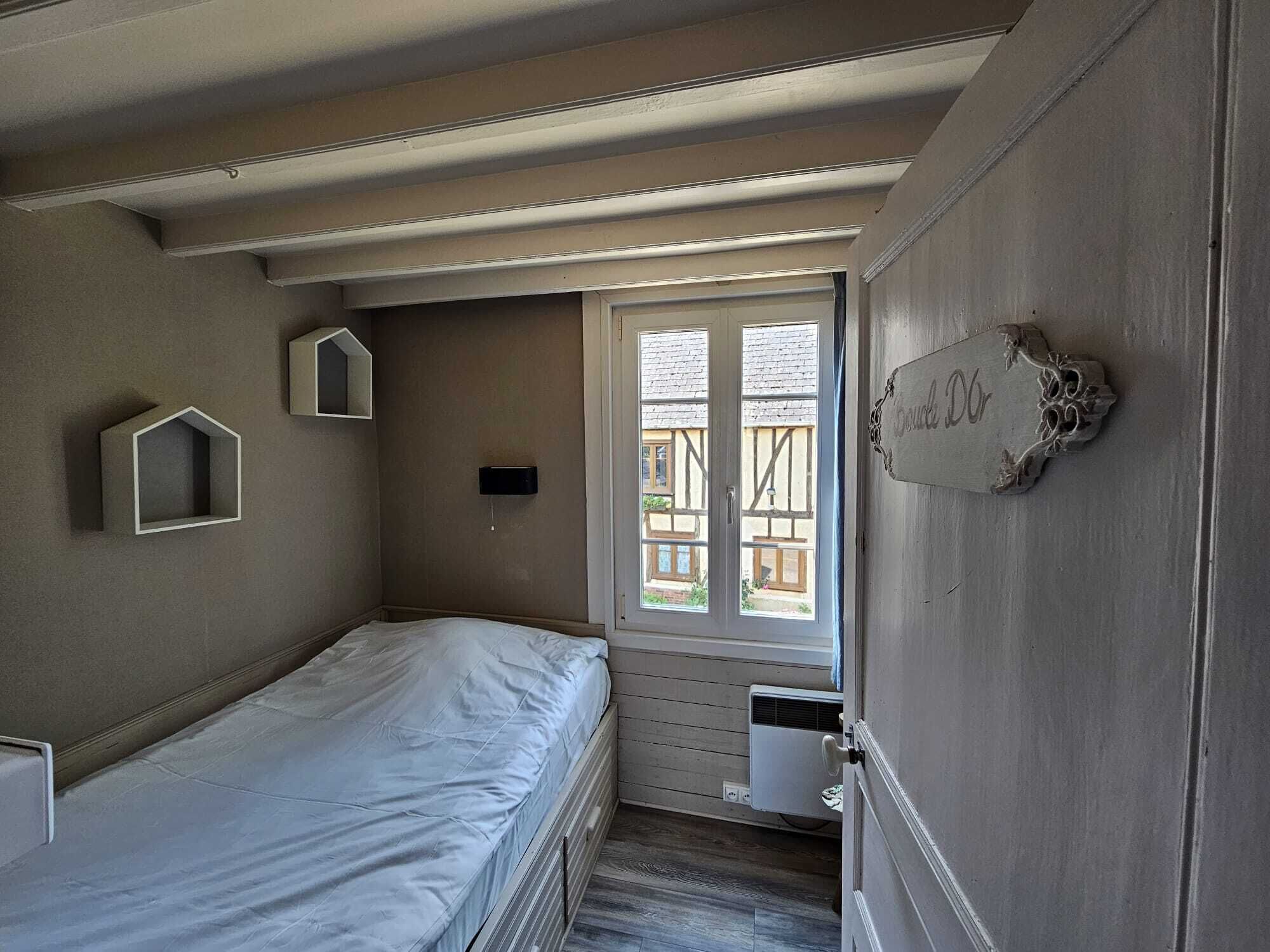A small, cozy room with a single bed, a small mirror, and a window with a view of the outside.