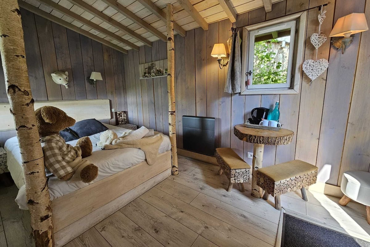 Een gezellig kamer in chaletstijl met een bed, een klein tafeltje en een raam met uitzicht op groen.