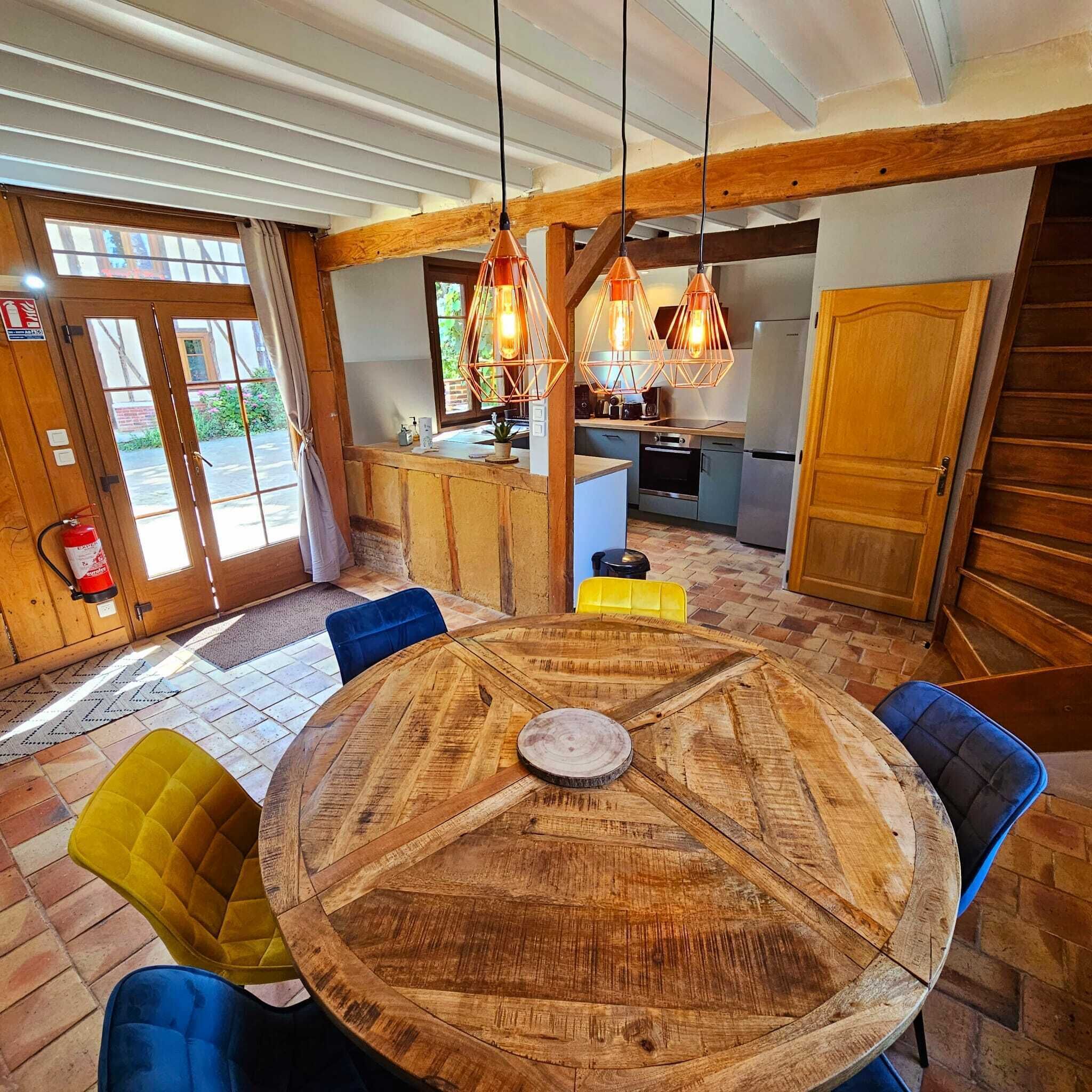 A dining area with a round wooden table, blue and yellow chairs, and copper pendant lights.