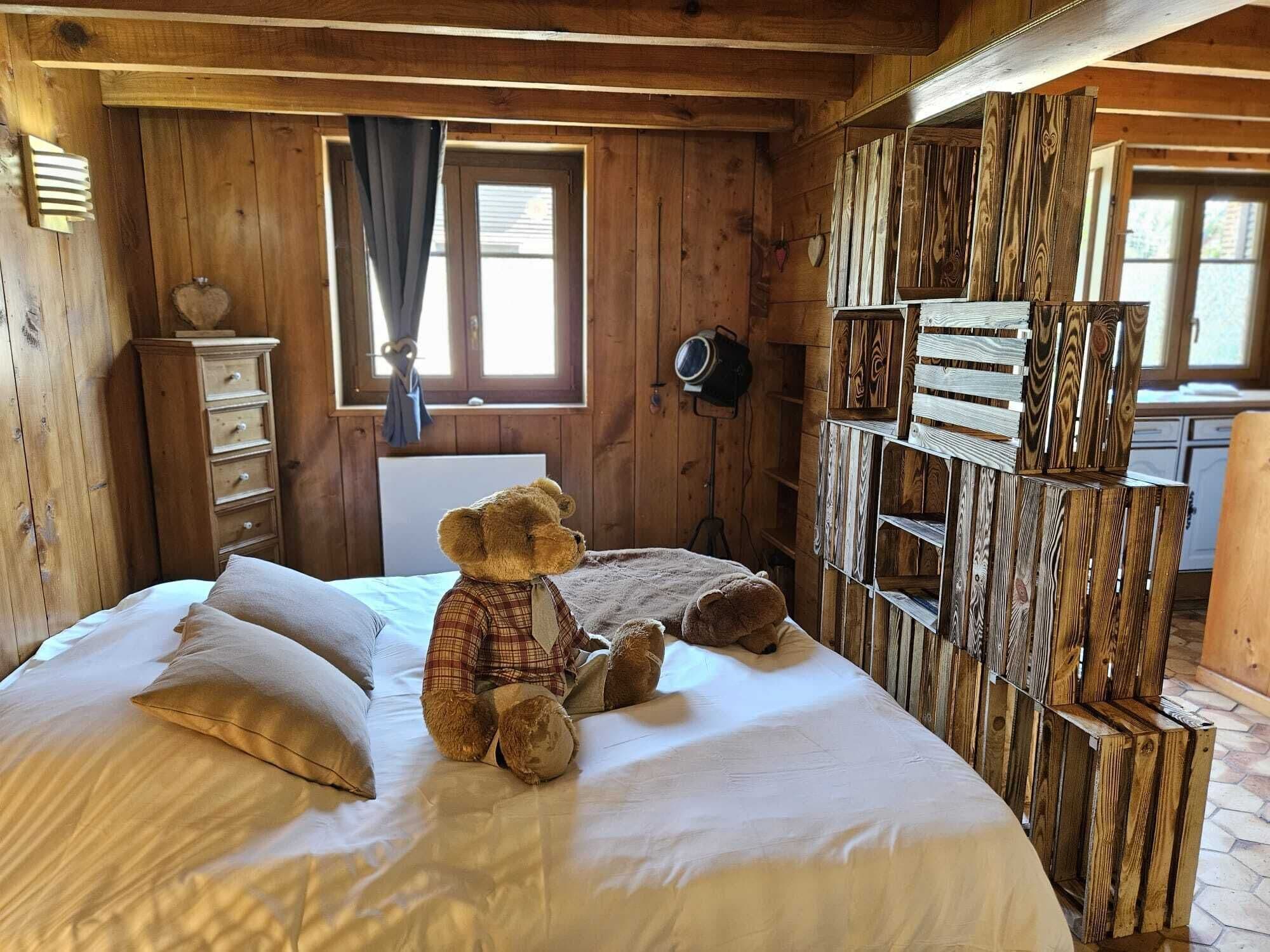 Une pièce de cabane en bois comprenant un lit, une commode, une fenêtre avec des rideaux et un mur recouvert de planches de bois.