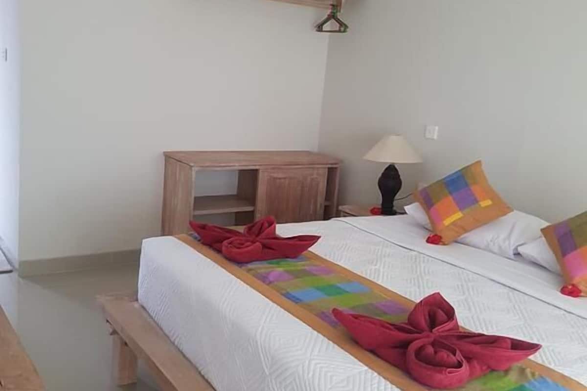A hotel room with a large bed, a wooden bench, a small table, a hanging shelf, and a wall-mounted air conditioner.