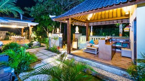 Een goed verlicht terras buiten met een houten terras, zithoekjes en een pad van stenen.