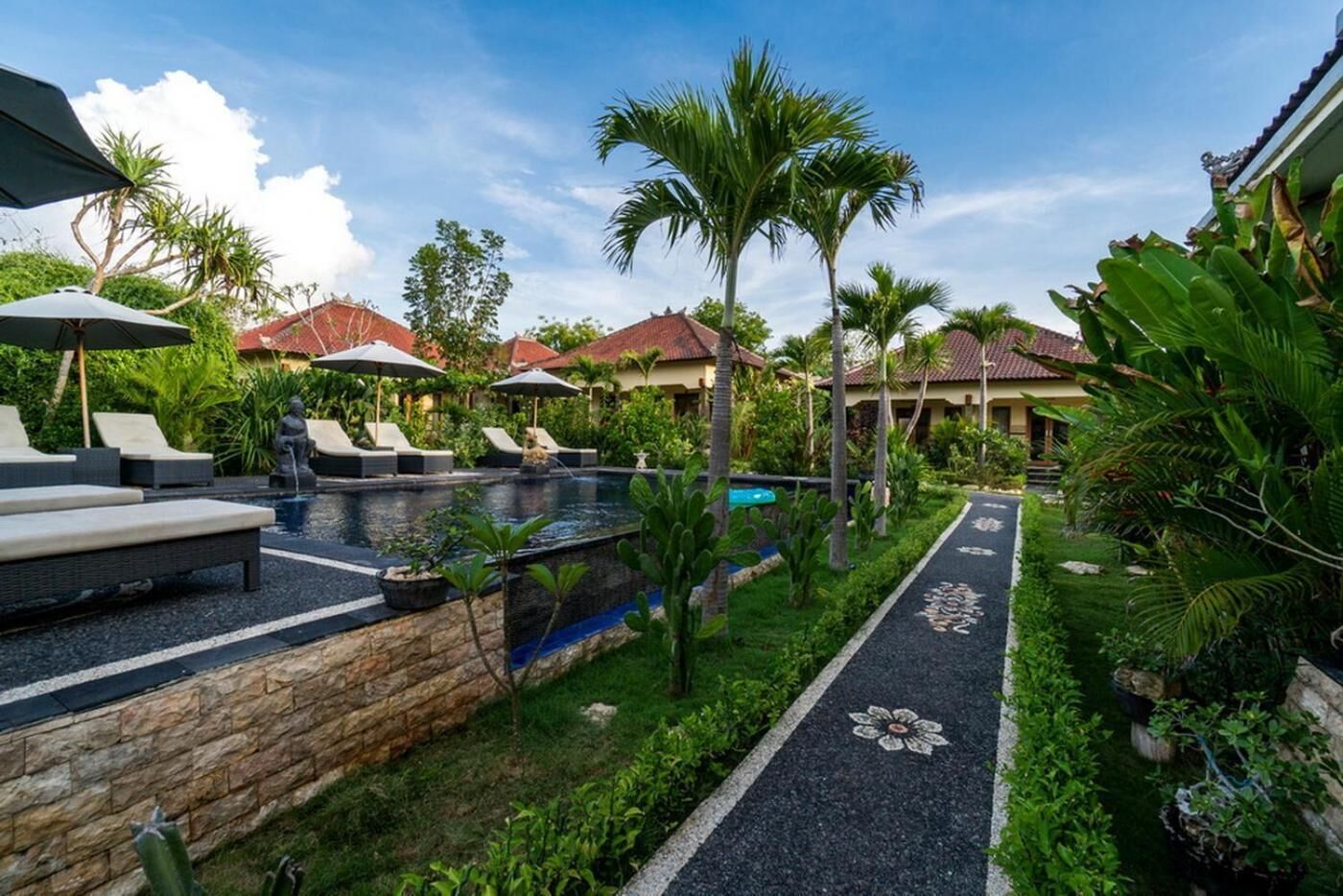 A pool area with lounge chairs and umbrellas, surrounded by palm trees and a stone wall.