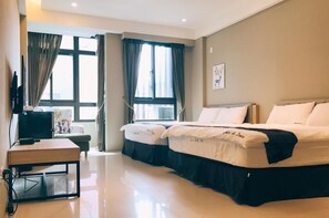 Habitación de hotel con dos camas, un escritorio, un televisor y ventanas grandes con cortinas.