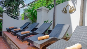 A row of wicker lounge chairs with cushions, arranged on a tiled patio with a white wall and decorative wall art in the background. - Villa Silk Road Hotel (Phnom Penh)