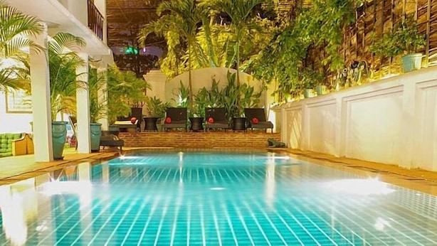 An indoor swimming pool with a tiled floor, surrounded by potted plants and a seating area with chairs and tables. - Villa Silk Road Hotel (Phnom Penh)