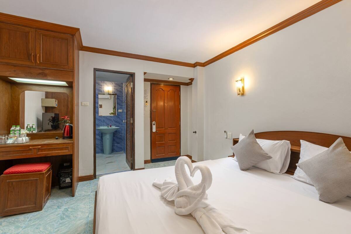 A hotel room with a bed, a desk, a mirror, a bathroom visible through an open door, and a wall-mounted light fixture.