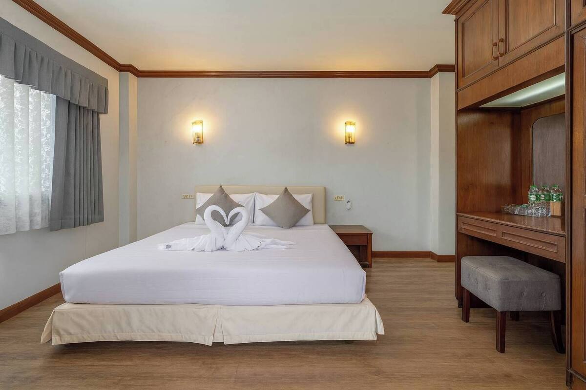 A hotel room with a large bed, two bedside tables, a wooden wardrobe, and a bench.