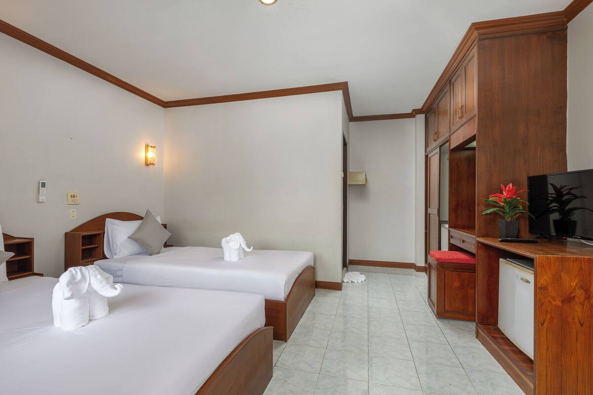 A hotel room with two beds, a wooden desk, a television, and a wall-mounted light fixture.