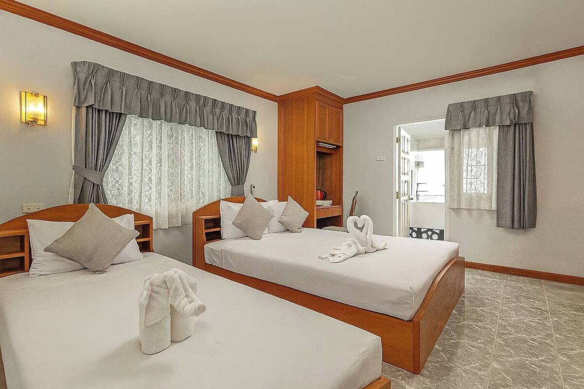 A hotel room with two beds, wooden headboards, a wardrobe, a vanity, and a mirror.