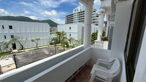 A balcony with a view of a parking lot, a white building, and a mountain in the background. - Break Point Patong Hotel (Patong)