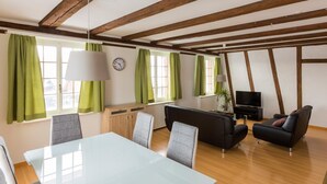 A modern living room with a glass table, grey chairs, a black sofa, and a TV. - Stars and Stripes - Motel Steighof (Brutten)