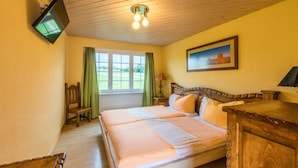 A bedroom with a bed, a television mounted on the wall, a painting, and a window with curtains. - Stars and Stripes - Motel Steighof (Brutten)