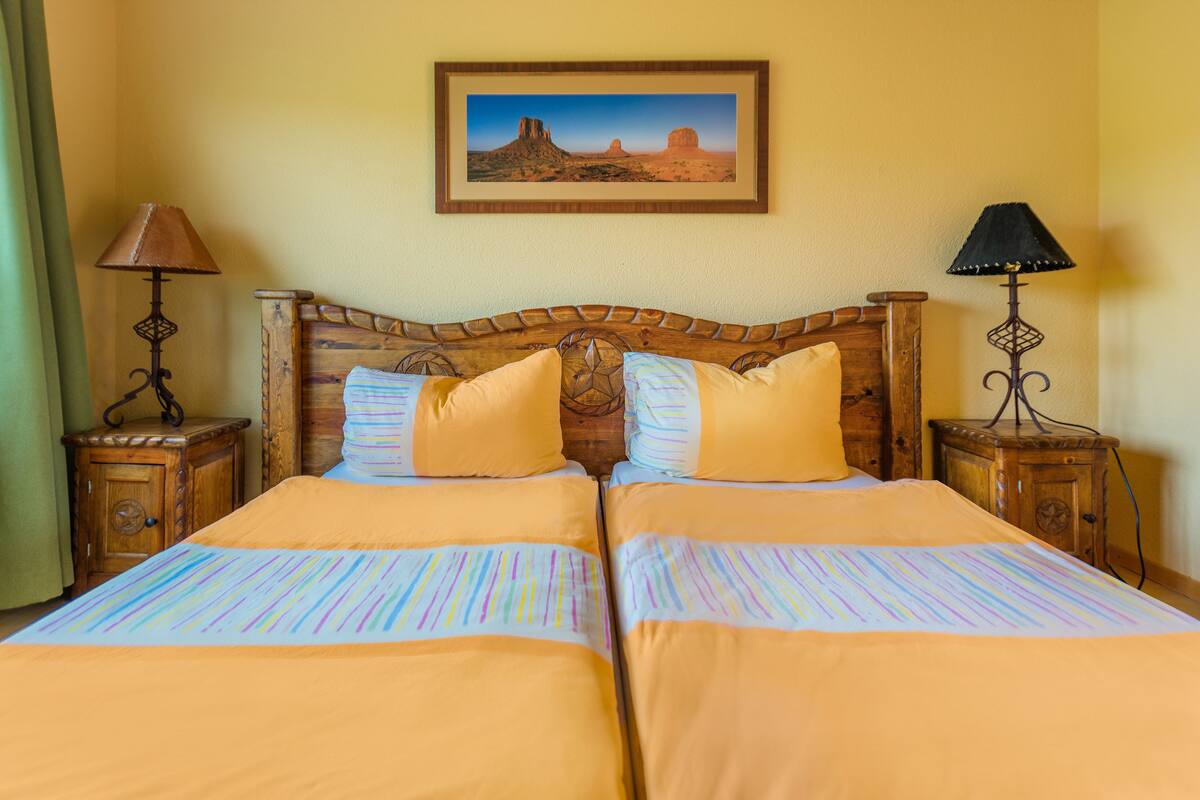 A double bed with striped bedding, two bedside tables with lamps, and a framed desert landscape painting on the wall.
