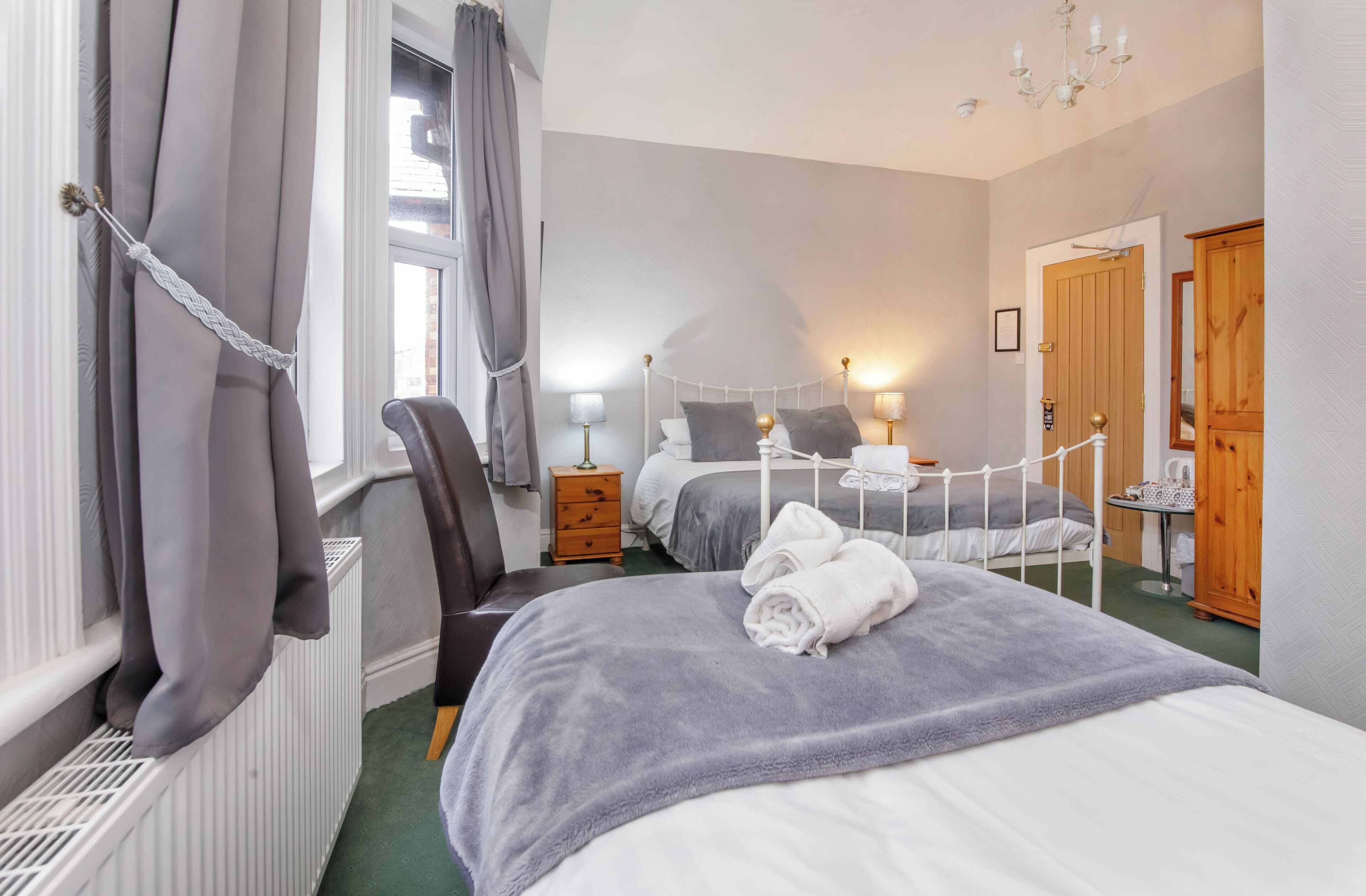 A bedroom with a bed, two bedside tables, a chair, a wardrobe, and a window with curtains.