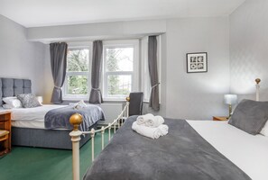 A hotel room with two beds, a large window with curtains, a framed picture on the wall, and a bedside table with a lamp. - St Mary's Guest House  (York)