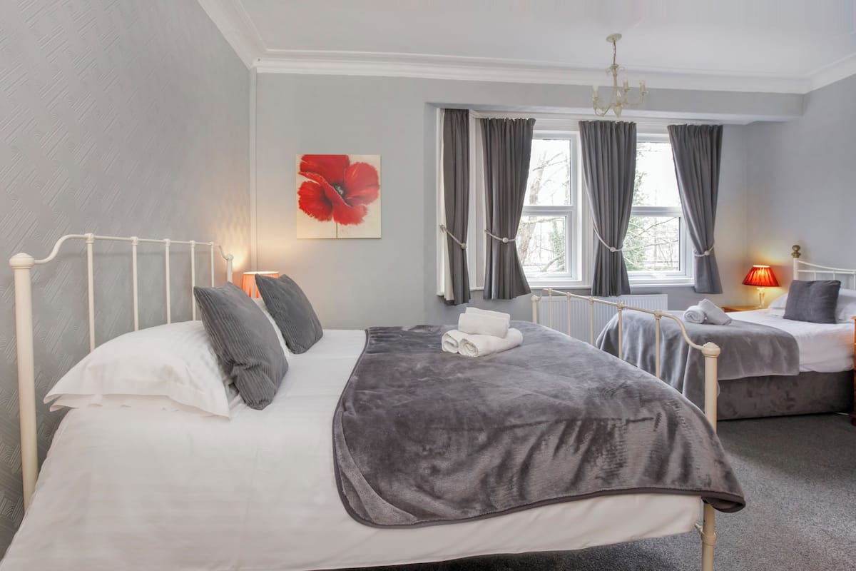 A bedroom with two beds, a radiator, a chandelier, and a window with curtains.