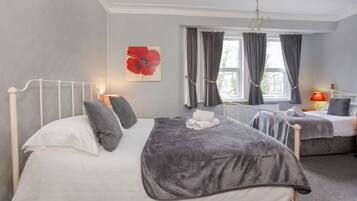 A bedroom with two beds, a radiator, a chandelier, and a window with curtains.