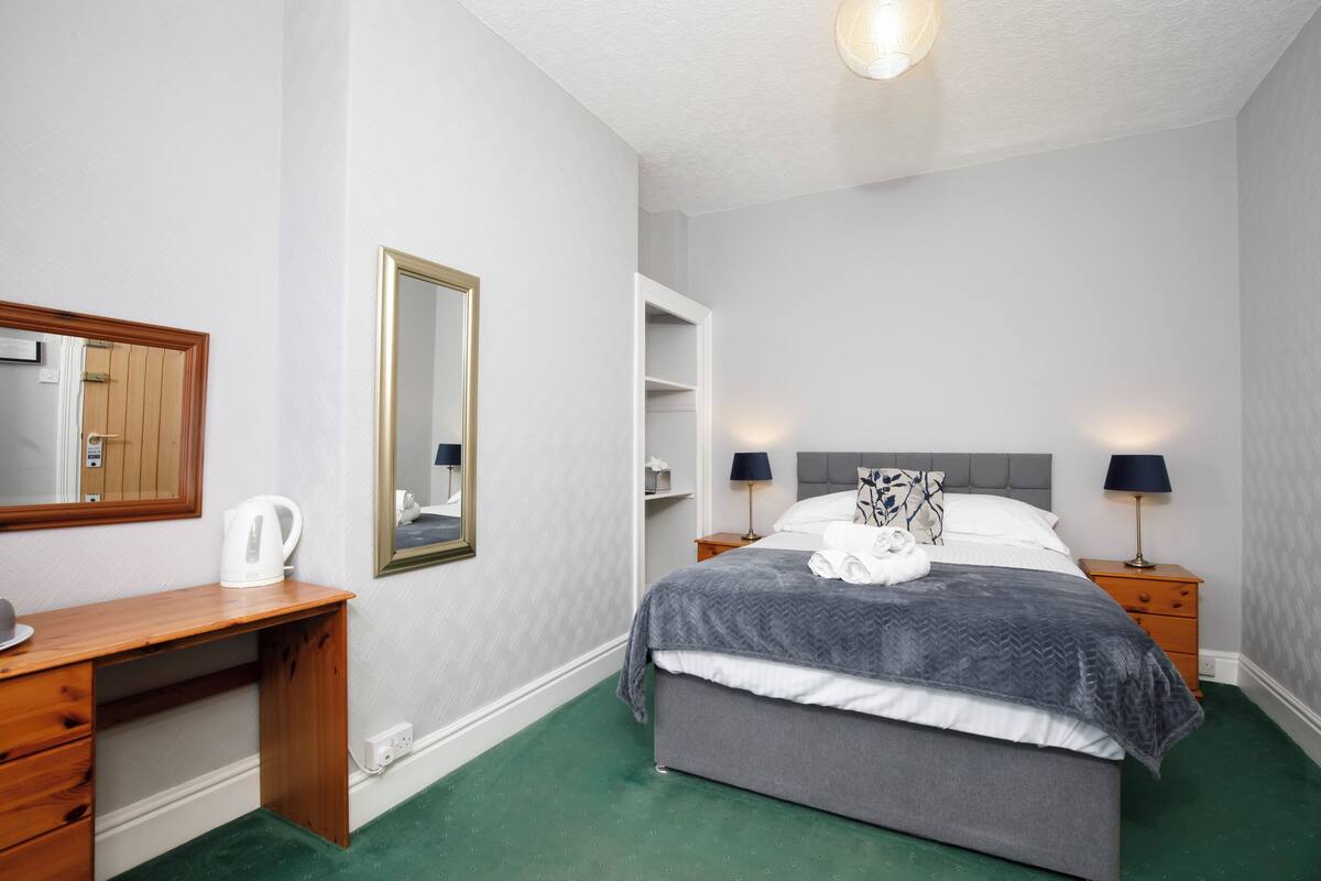 A bedroom with a bed, bedside tables, a desk, a mirror, and a wardrobe.