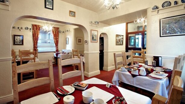 A dining area with wooden chairs, tables set for a meal, and a chandelier. - St Mary's Guest House  (York)