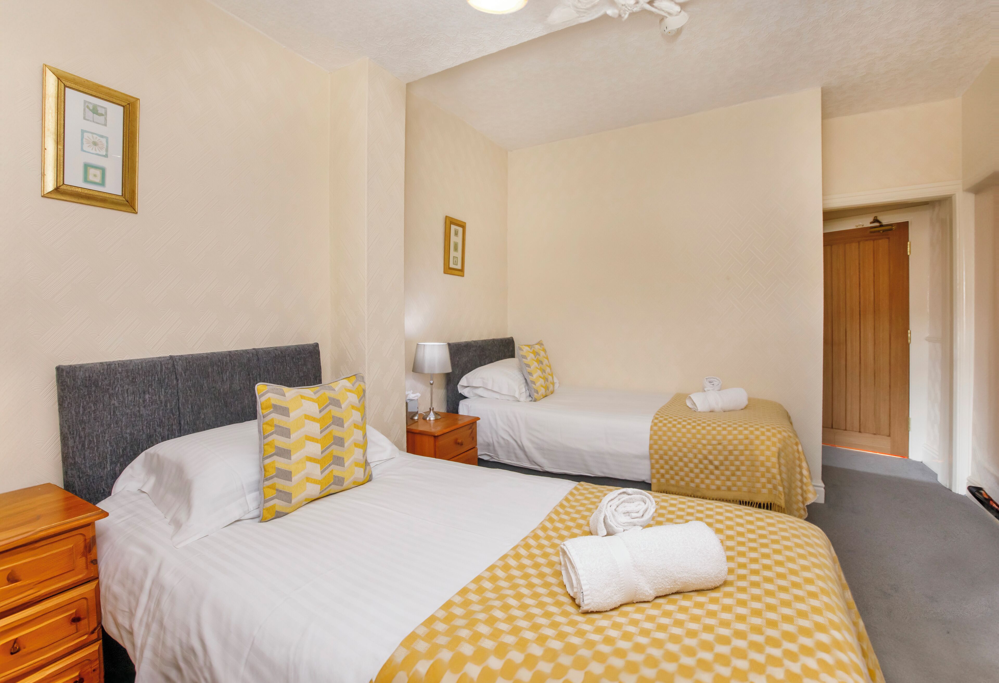 A hotel room with two beds, a wooden nightstand, a lamp, and a door leading to a bathroom.