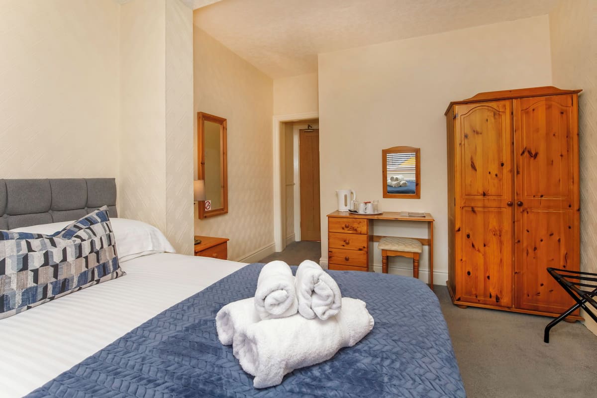A hotel room with a bed, a desk, a wardrobe, and a mirror.