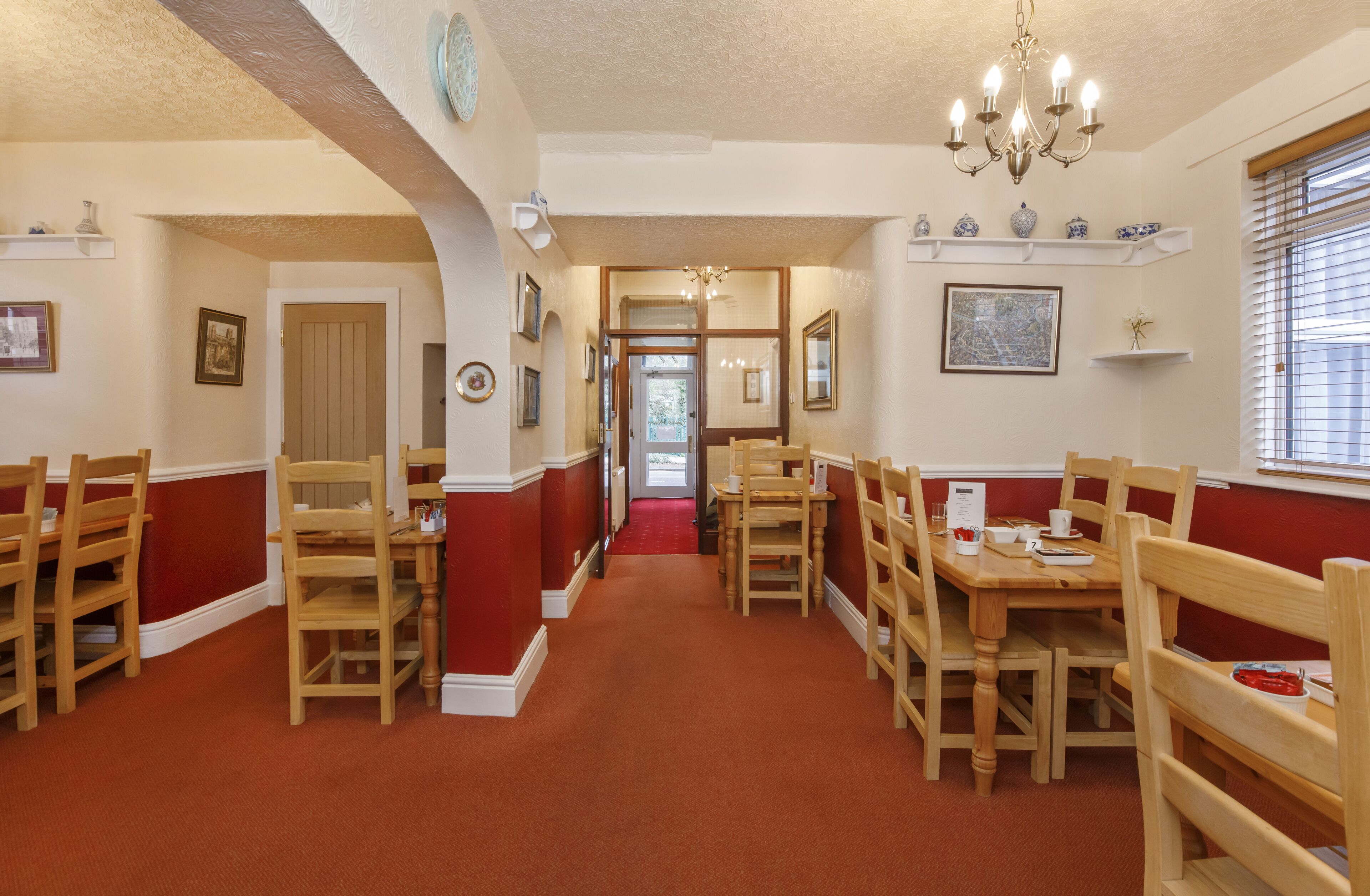 A dining area with wooden tables and chairs, a chandelier, and red and white walls.