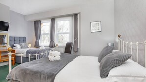 A hotel room with two beds, a TV, a desk, and a window with curtains. - St Mary's Guest House  (York)