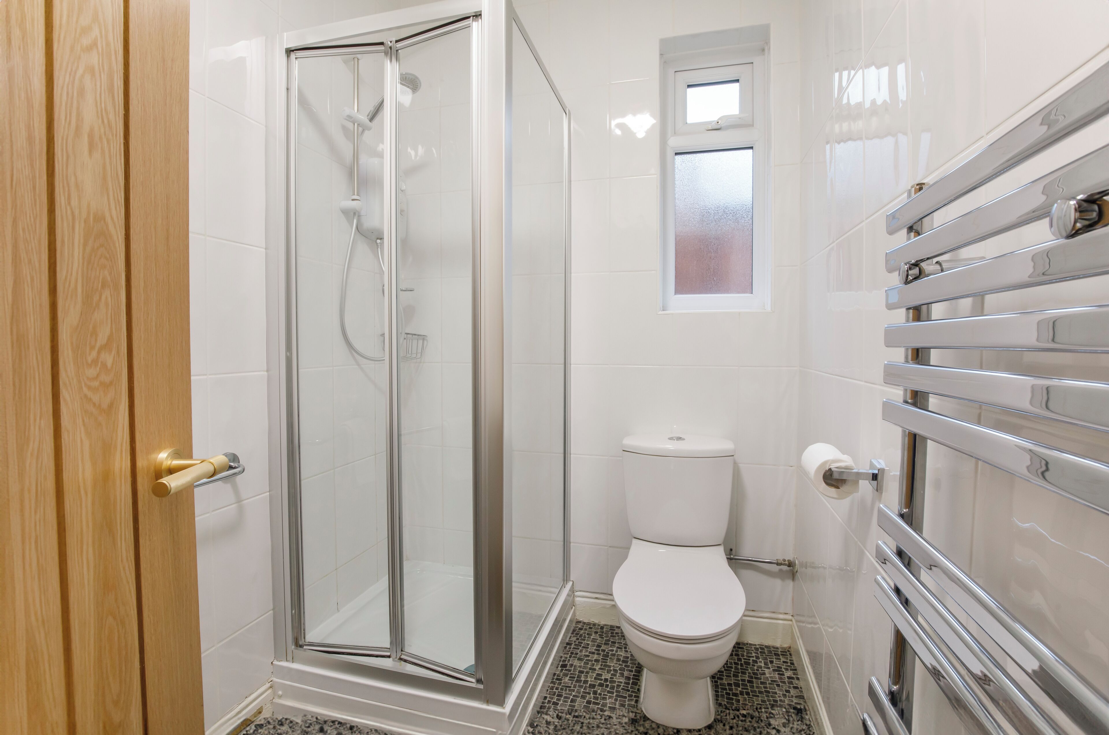 Une salle de bain avec une douche à parois de verre, des toilettes blanches et un porte-serviettes.