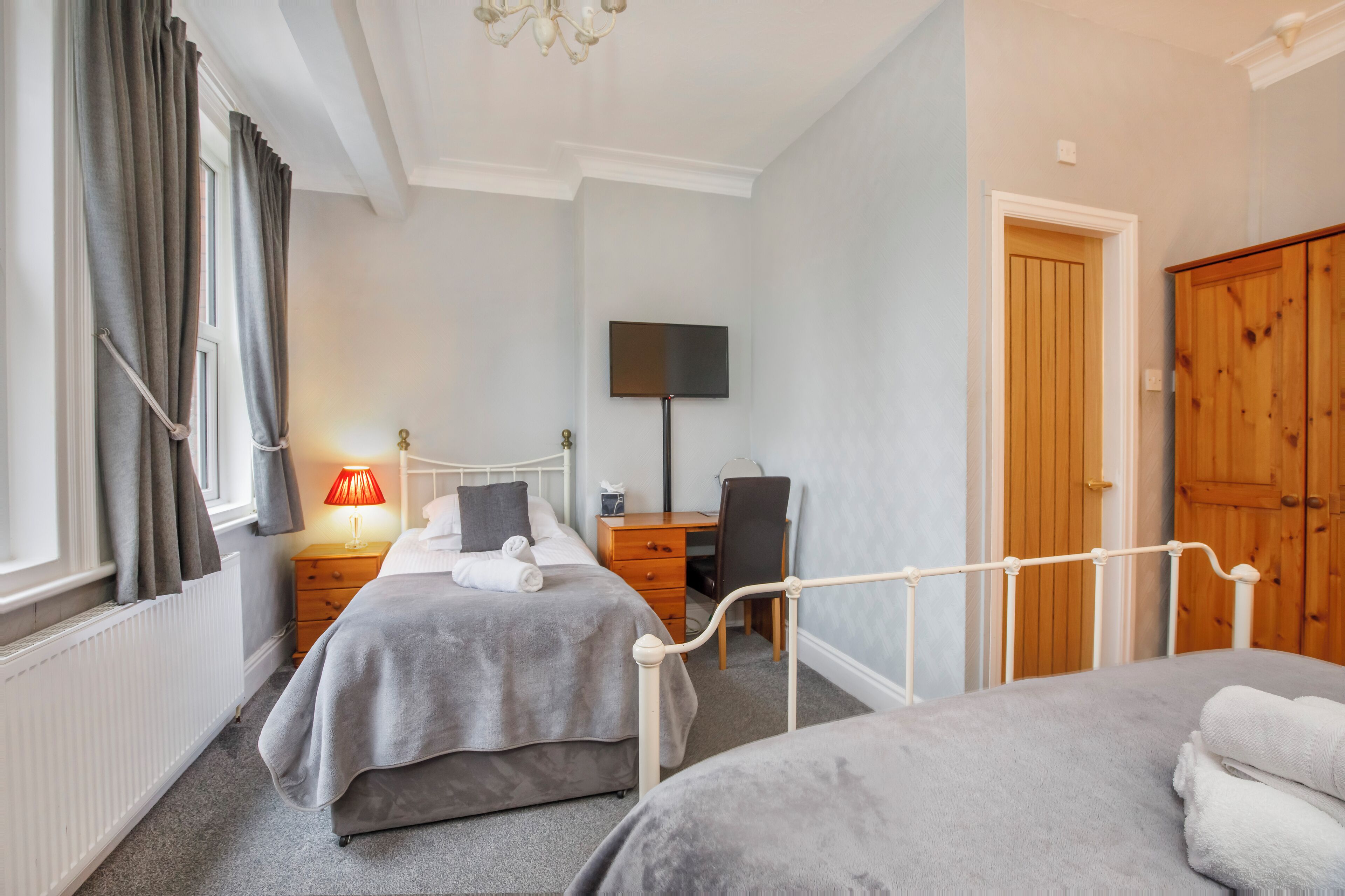 A bedroom with two beds, a desk, a chair, a TV, and a wardrobe.
