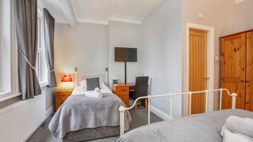 A bedroom with two beds, a desk, a chair, a TV, and a wardrobe.