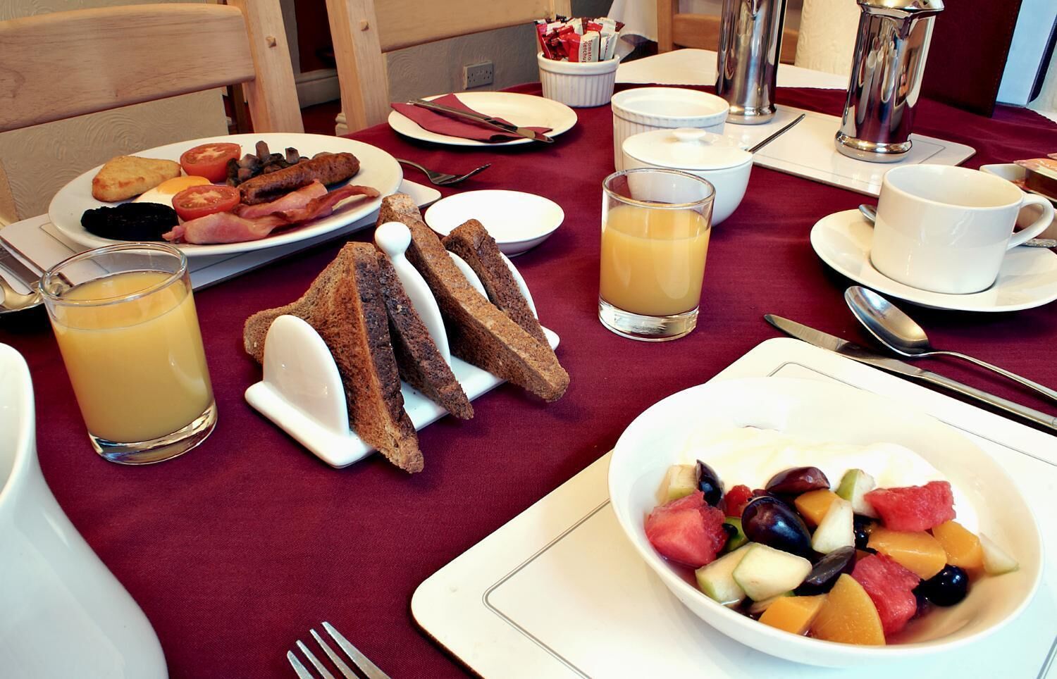 A breakfast setting with toast, fruit, and juice on a table.