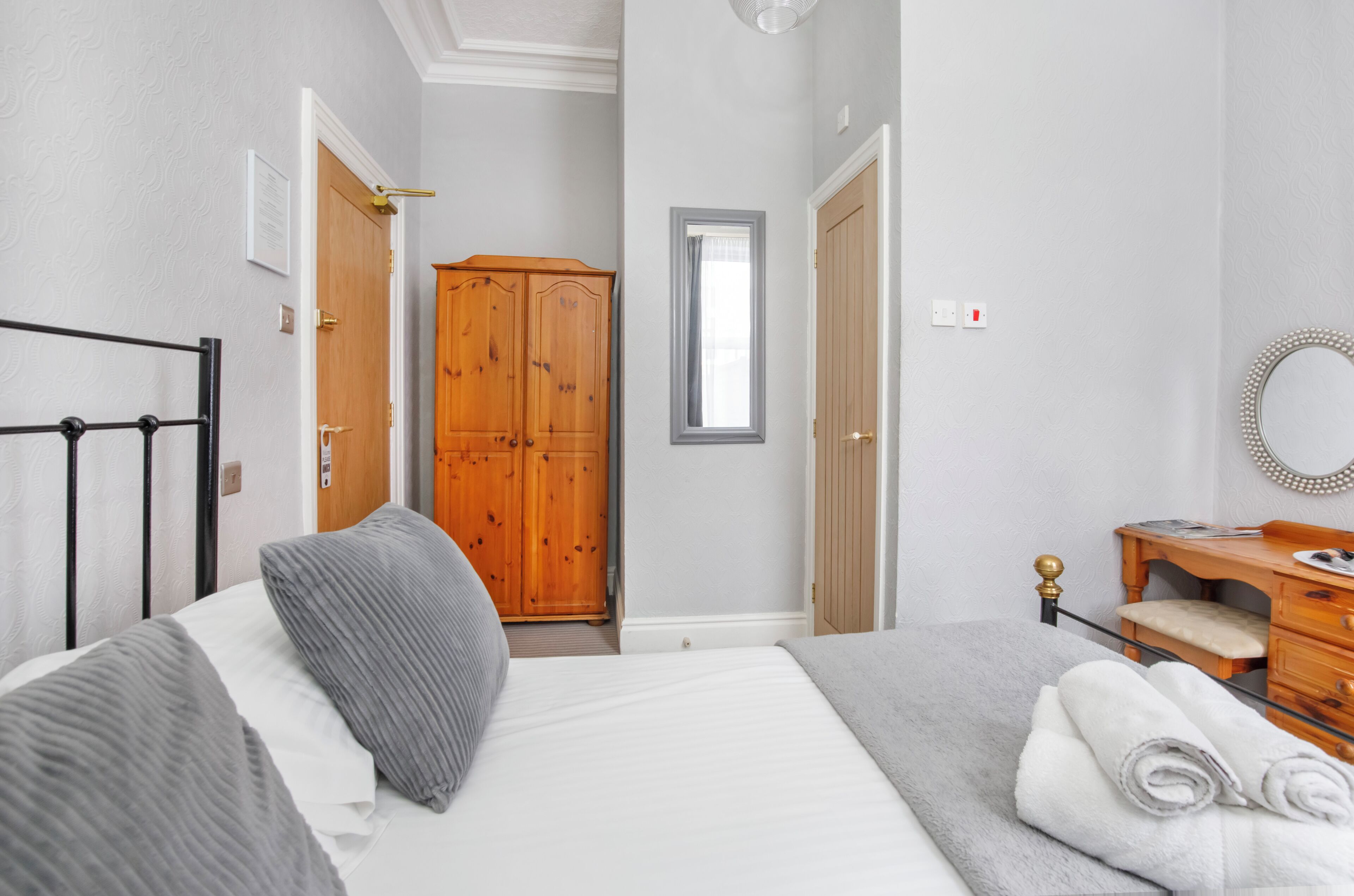 A bedroom with a bed, a wooden wardrobe, a mirror, and a dresser.