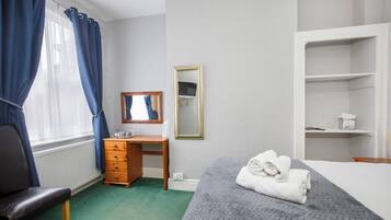 A bedroom with a bed, a wooden dresser, a desk, a mirror, and a radiator.