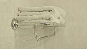A bathroom with a towel rack holding three folded towels. - Abbey Lodge Hotel (High Wycombe)