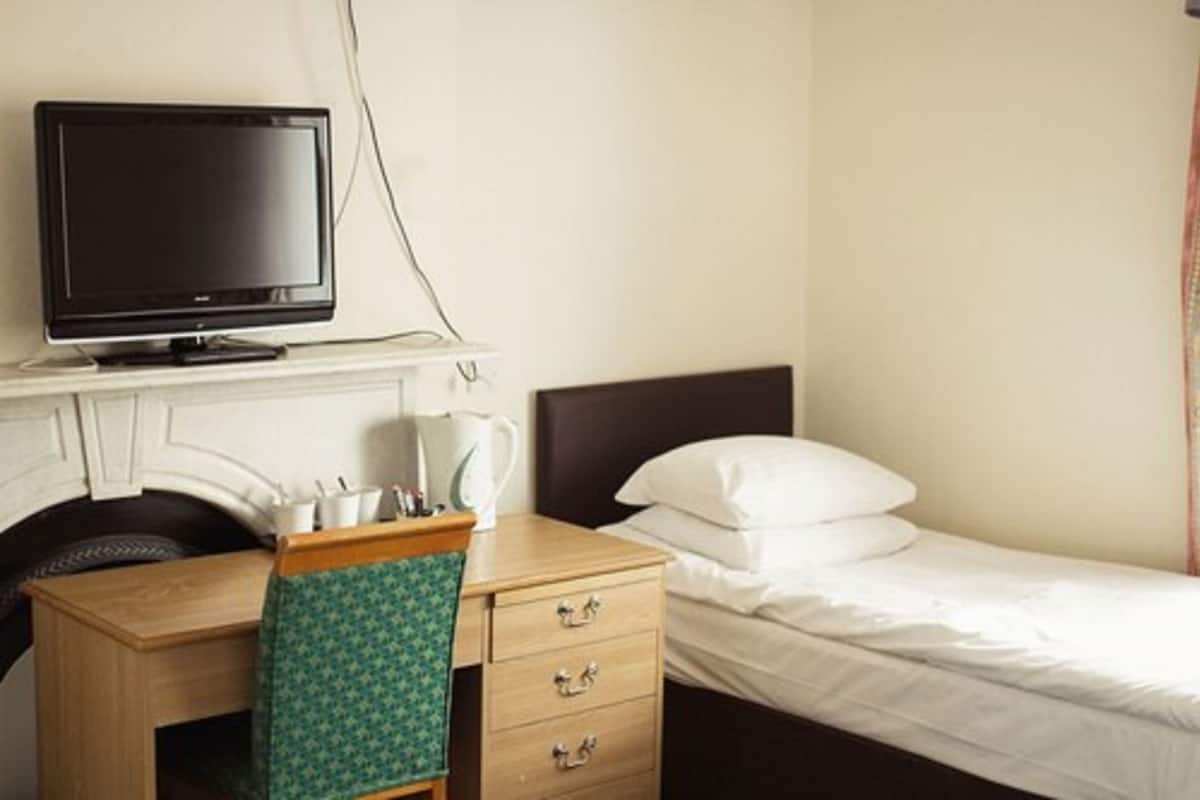 A hotel room with a bed, a desk with a television, and a coffee maker.