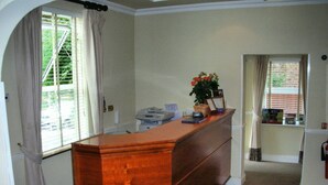 A room with a wooden desk, a printer, and a potted plant. There is a window with curtains and a view of greenery outside. - Abbey Lodge Hotel (High Wycombe)