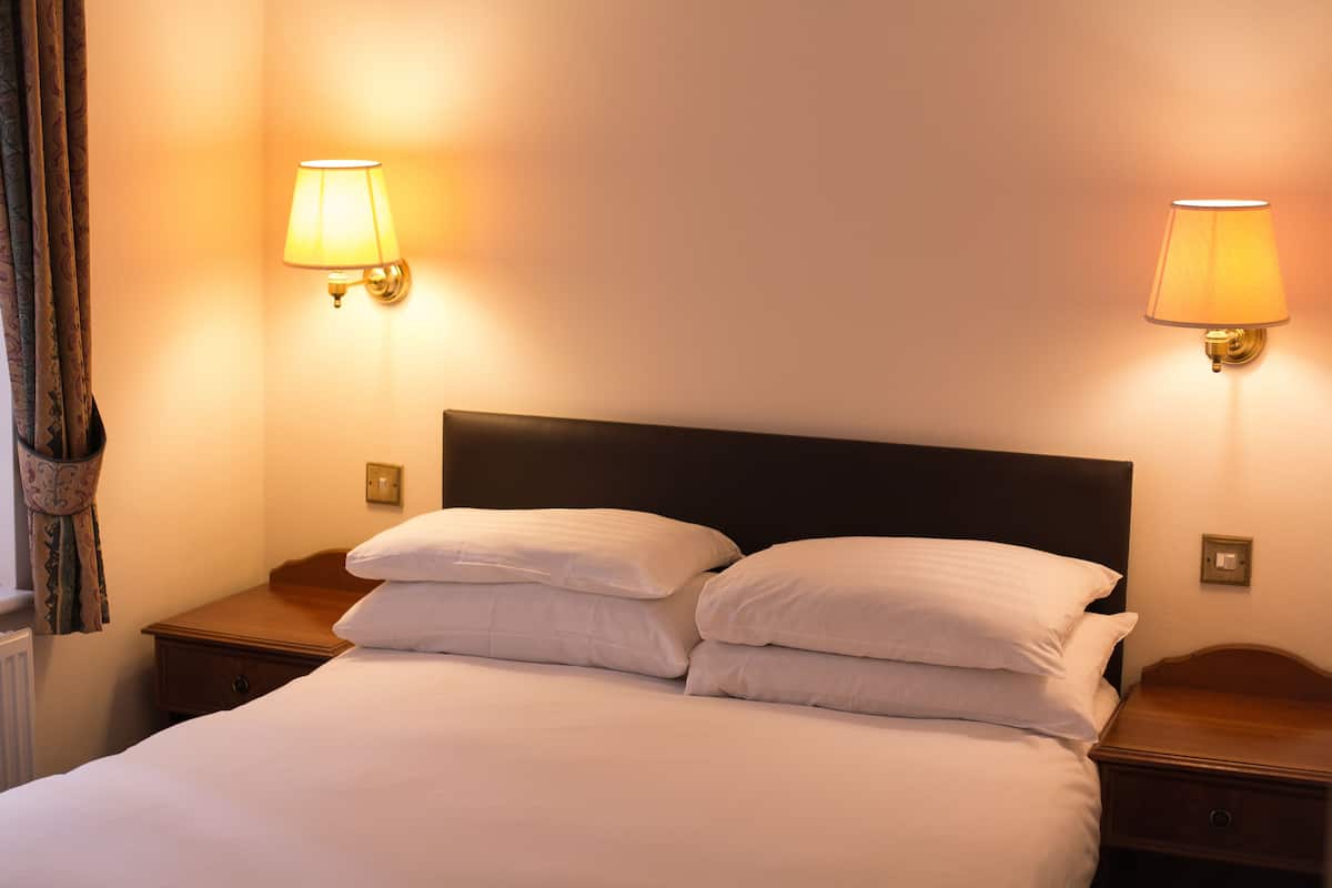 A neatly made bed with two pillows, a wooden nightstand, and two wall-mounted lamps.