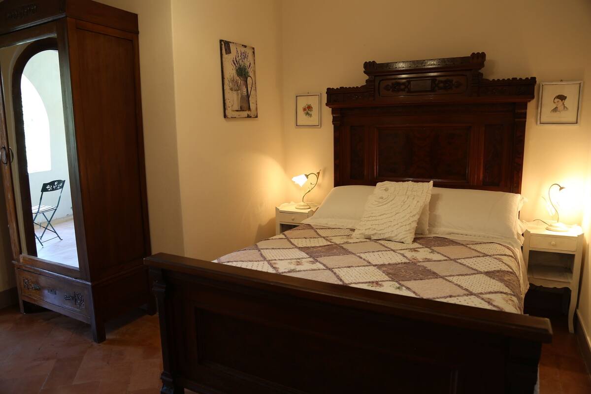 Un dormitorio con una cama de madera, dos mesitas de noche, un aparador, un tocador y una puerta con un espejo.
