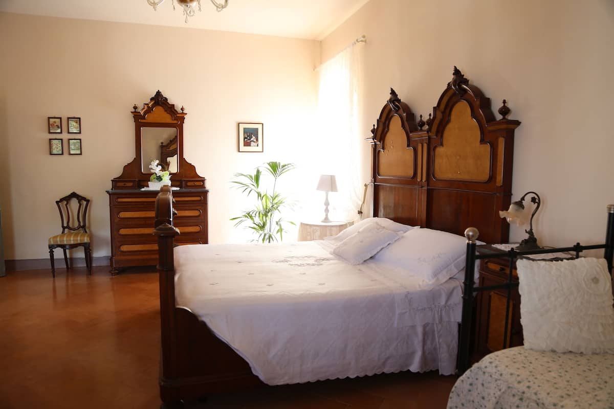 Un dormitorio con una cama grande de madera, un aparador de madera, una silla, una mesita de noche con una lámpara y una planta en maceta.